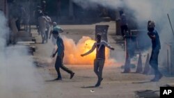 A tear gas shell fired by an Indian policeman explodes behind Kashmiri protesters during a protest in Srinagar, Indian controlled Kashmir, June 16, 2017. 