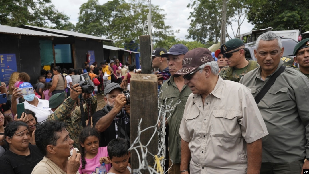 El presidente electo panameño, José Raúl Mulino, habla con un migrante venezolano (izq.) y otros migrantes en un campamento después de cruzar caminando el Tapón del Darién desde Colombia, en Lajas Blancas, Panamá, el viernes 28 de junio de 2024. 