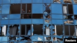 Muškarci gledaju kroz razbijeni prozor poslovnog i zabavnog centra teško oštećenog ruskim vojnim udarom u Harkovu