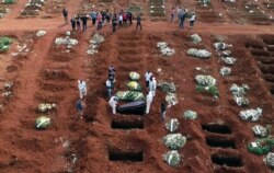 FILE - Cemetery workers wearing protective gear lower the coffin of a person who died from complications related to COVID-19 into a gravesite at the Vila Formosa cemetery in Sao Paulo, Brazil, Apr. 7, 2021.