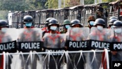 In this Friday, Feb. 19, 2021 file photo, military trucks with soldiers inside are parked behind police standing guard behind a road barricade in Mandalay, Myanmar.