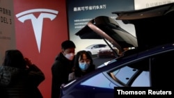 Visitors wearing face masks check a China-made Tesla Model Y sport utility vehicle (SUV) at the electric vehicle maker's showroom in Beijing, Jan. 10, 2021.