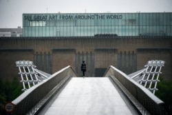 A woman walks on a nearly deserted Millennium Bridge as the rain falls, on the sixth week of lockdown due to the coronavirus outbreak, in London, April 28, 2020.