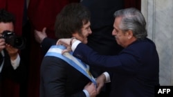 Javier Milei recebe a faixa presidencial do seu antecessor Alberto Fernandez na cerimónia de posse como Presidente da Argentina no Congresso, Buenos Aires, 10 dezembro 2023 (By ALEJANDRO PAGNI / AFP)