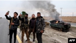 Armed men pose for pictures near a burning military vehicle belonging to the Syrian regime forces and seized by anti-government forces, in the Hama governorate, Dec. 7, 2024.