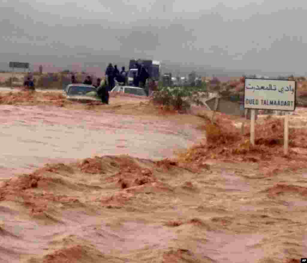 Warga di kota Guelmim, Maroko berdiri di atas kendaraan sementara terjebak oleh banjir, yang menewaskan sedikitnya 17 orang di kawasan itu.