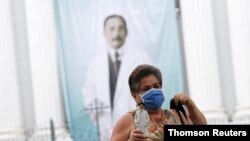 Una mujer sostiene una figura de José Gregorio Hernández mientras caminaba frente a una iglesia en Caracas.