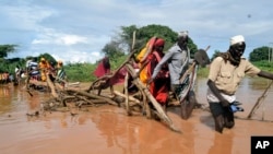 FILE —Residents of Chamwana Muma village walk through flood water after using a makeshift bridge to cross the swollen River Tana, in Tana Delta, Kenya, on Wednesday Nov. 15, 2023. 