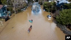 FILE - People take their boats into the water on the flooded River Road in Guerneville, Calif., Feb. 28, 2019.