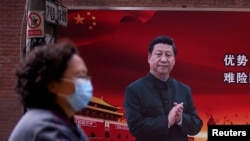 FILE PHOTO: A woman wearing a protective mask is seen past a portrait of Chinese President Xi Jinping on a street as the country is hit by an outbreak of the coronavirus, in Shanghai, China March 12, 2020. REUTERS/Aly Song/File Photo