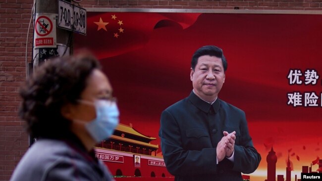 资料照片:一名戴口罩的女士经过有习近平像的上海街头标语牌。(2020年3月12日)