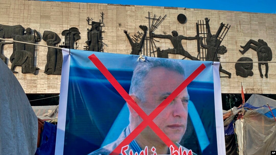 A poster with a defaced picture of Mustafa Kadhimi, Iraq's intelligence chief and new prime minister-designate, is shown in Tahrir Square, Baghdad, Iraq, Saturday, April 11, 2020. 