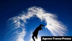 A woman throws hot water from a thermos bottle into the cold air making its three phases visible - liquid, gas, solid - as the smallest droplets cool and evaporate in a dramatic cloud before they reach the ground as snow, in Berlin on a sunny but frosty Boxing Day.
