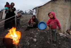 FILE - Displaced Syrian women and children, who fled from southern Idlib, gather around a fire in Afrin, Syria, Feb. 6, 2020.