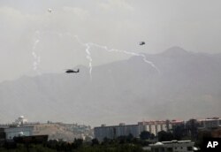 Anti-missile decoy flares are deployed as U.S. Black Hawk military helicopters and a dirigible balloon fly over the city of Kabul, Afghanistan, Aug. 15, 2021.