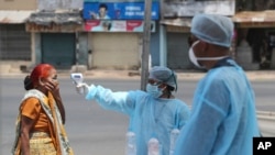 An Indian health worker checks the temperature of a woman during lockdown to prevent the spread of new coronavirus in Ahmedabad, India, Wednesday, April 8, 2020.