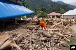 A boy crawls on logs swept into a neighborhood affected by a flash flood in Pesisir Selatan, West Sumatra, Indonesia, Wednesday, March 13, 2024. (AP Photo/Mavendra JR)