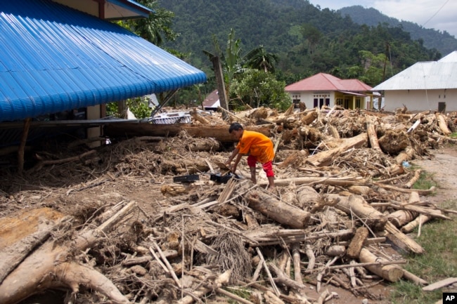 A boy crawls on logs swept into a neighborhood affected by a flash flood in Pesisir Selatan, West Sumatra, Indonesia, Wednesday, March 13, 2024. (AP Photo/Mavendra JR)