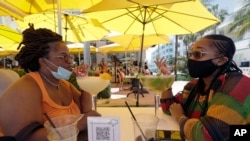 Anita Anderson, a la izquierda, de Grand Rapids, Michigan, y su sobrina Tawnya Heggins de Houston, conversan mientras cenan frente a un restaurante en Miami Beach, el famoso South Beach de Florida, el viernes 26 de junio de 2020. 