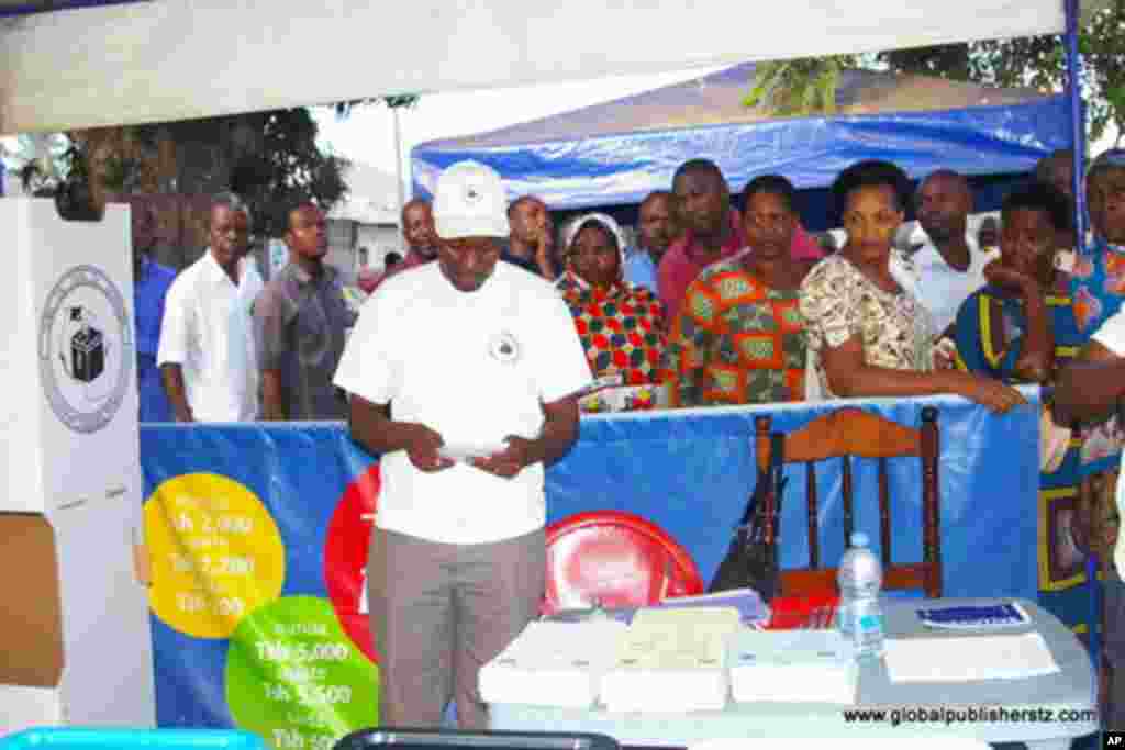 Msimamizi wa kituo cha kupiga kura akitayarisha vifaa vya kupiga kura huku wapiga kura wakisimama kusubiri kufunguliwa kwa kituo.