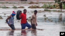 (FILE) People walk on a road swept by flooding waters in Chikwawa, Malawi.
