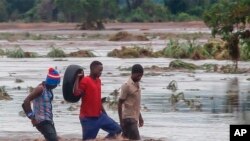 FILE — People walk on a road swept by flooding waters in Chikwawa, Malawi, Tuesday Jan. 25, 2022. Mozambique, Madagascar and Malawi are counting the deaths and damage by tropical storm Ana and more than a week of heavy rains across southern Africa.