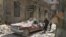 People walk near a damaged vehicle after an airstrike Sunday in the rebel-held besieged al-Qaterji neighborhood of Aleppo, Syria, Oct. 17, 2016. 