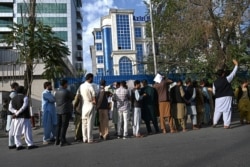 People queue as they wait for their turn to withdraw money from an ATM in front of a bank along a roadside in Kabul, Afghanistan, Aug. 21, 2021.