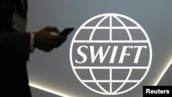 FILE - A man using a cellphone passes the logo of global secure financial messaging services cooperative SWIFT, Toronto, Canada.