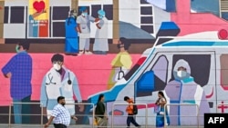 Pedestrians walk past a wall mural promoting awareness on using face masks, in Bengaluru on January 6, 2025,