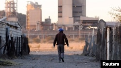 FILE - A township resident walks past Lonmin's Marikana platinum mine, June 13, 2014. 