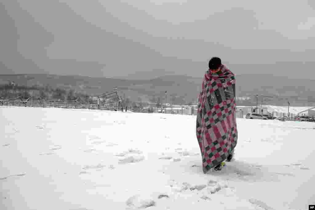 A migrant wrapped in a blanket, walks through the snow at the Lipa camp northwestern Bosnia, near the border with Croatia, Dec. 26, 2020.