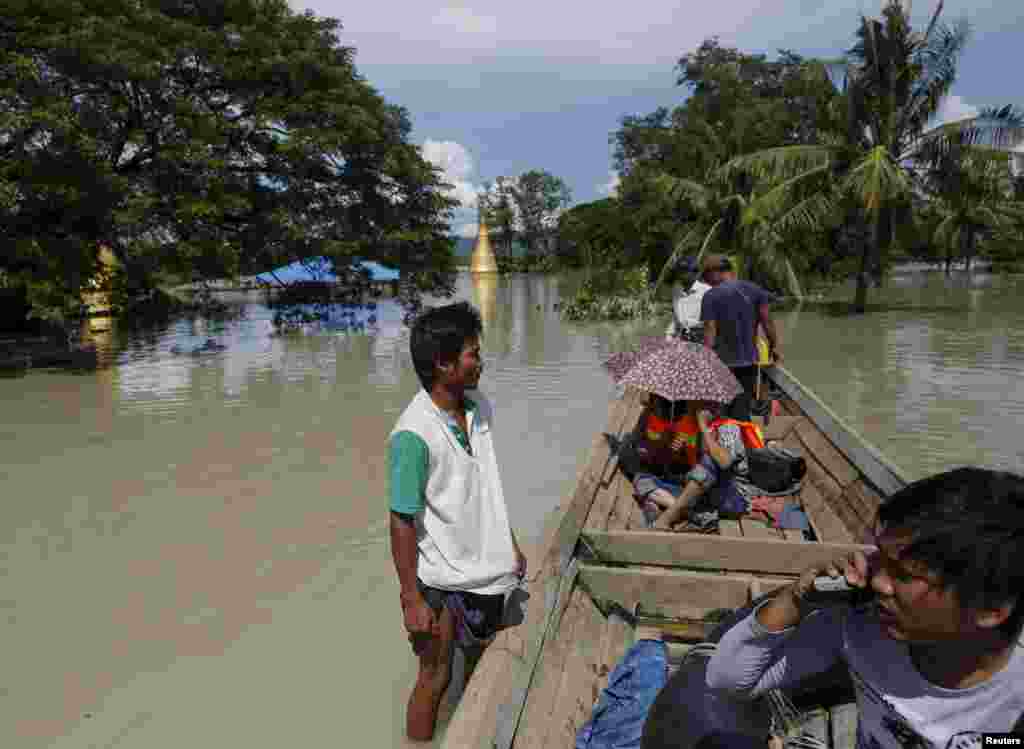 A boat man (left) stands on the roof of a flooded home next to a media boat in Kalay township, a village in the Sagaing region, northwestern Myanmar, Aug. 2, 2015.