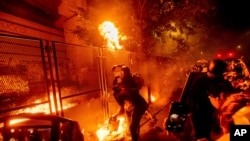 Protesters throw flaming debris over a fence at the Mark O. Hatfield United States Courthouse on Wednesday, July 22, 2020, in Portland, Ore. Following a larger Black Lives Matter Rally, several hundred demonstrators faced off against federal…