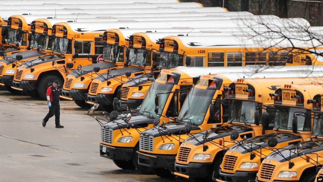 A worker passes public school buses parked at a depot in Manchester, New Hampshire, April 27, 2020. Children continue to be taught with remote learning while buildings are closed.