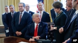 President Donald Trump looks over to Lockheed Martin Chairwoman, President and CEO Marillyn Hewson, right, before signing an executive order in the Oval Office of the White House on Friday, February 24, 2017. The executive order would establish regulatory reform officers and task forces within federal agencies a part of his push to cut federal government regulations. (AP Photo/Pablo Martinez Monsivais)