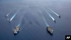 FILE - In this photo provided by U.S. Navy, the USS Ronald Reagan (CVN 76) and USS Nimitz (CVN 68) Carrier Strike Groups steam in formation, in the South China Sea, July 6, 2020.
