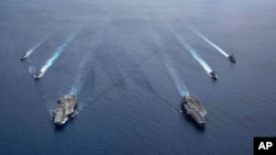 FILE - In this photo provided by U.S. Navy, the USS Ronald Reagan (CVN 76) and USS Nimitz (CVN 68) Carrier Strike Groups steam in formation, in the South China Sea, July 6, 2020.