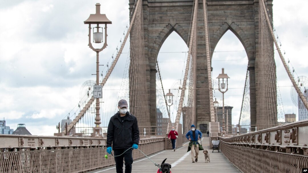 People wear facial masks for protection against the coronavirus as they walk their dogs on the Brooklyn Bridge, Friday, April 10, 2020, in New York. (AP Photo/Mary Altaffer)