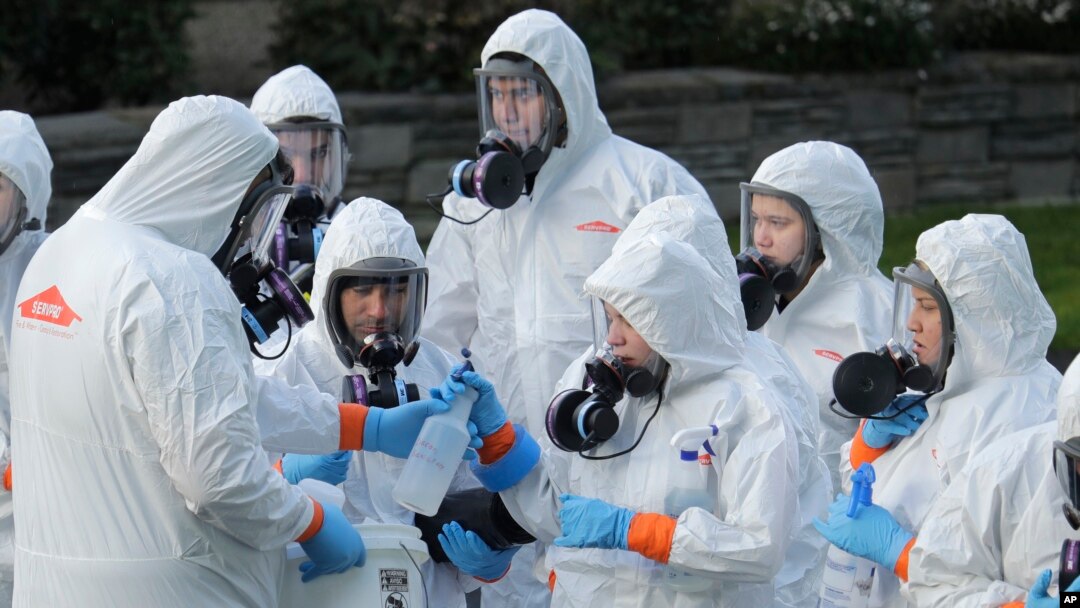 Workers from a Servpro disaster recovery team wearing protective suits and respirators are given supplies as they line up before entering the Life Care Center in Kirkland, Wash., to begin cleaning and disinfecting the facility, Wednesday, March 11, 2020…