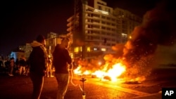 Protesters smoke water pipes in front burning tires that were set on fire to block a road, at Martyrs' Square, in downtown Beirut, Lebanon, March 6, 2021. 