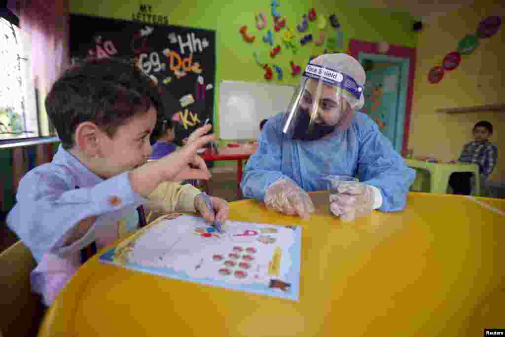 A teacher wearing a protective suit interacts with a child at a nursery after the government eased the coronavirus disease (COVID-19) restrictions in Amman, Jordan.