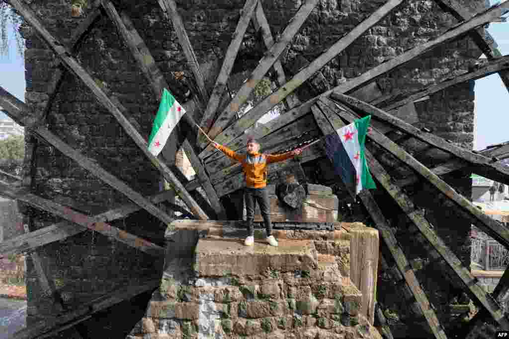 A boy waves the opposition Syrian flag as he stands in one of the water wheels, or norias, in Hama, after anti-government fighters captured the central city.