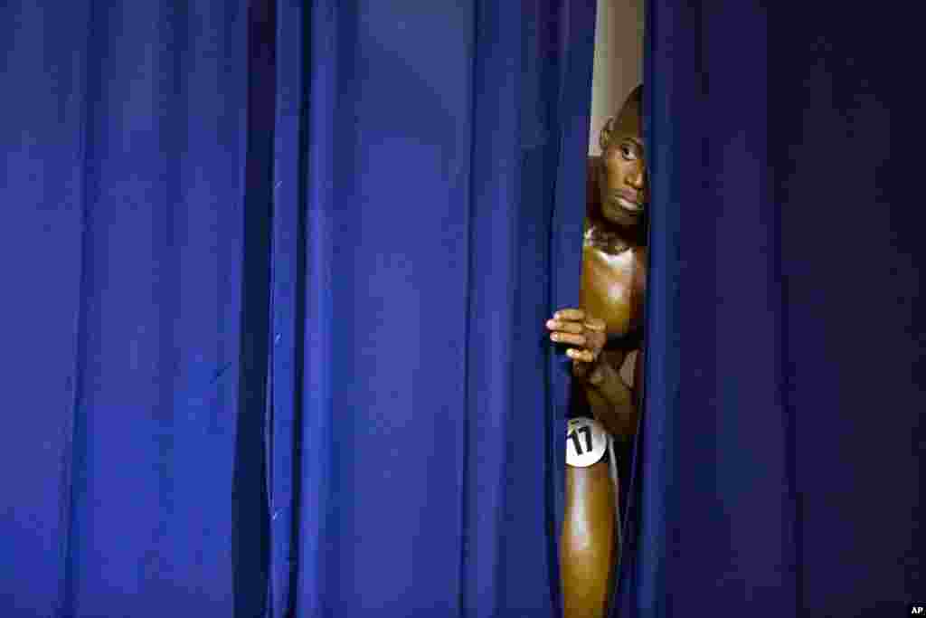 A Haitian bodybuilder peers from behind the curtain to watch his competitors perform at the Haiti Bodybuilding Classic, an event with Haitian and Dominican Republican athletes, in Port-au-Prince, Haiti.