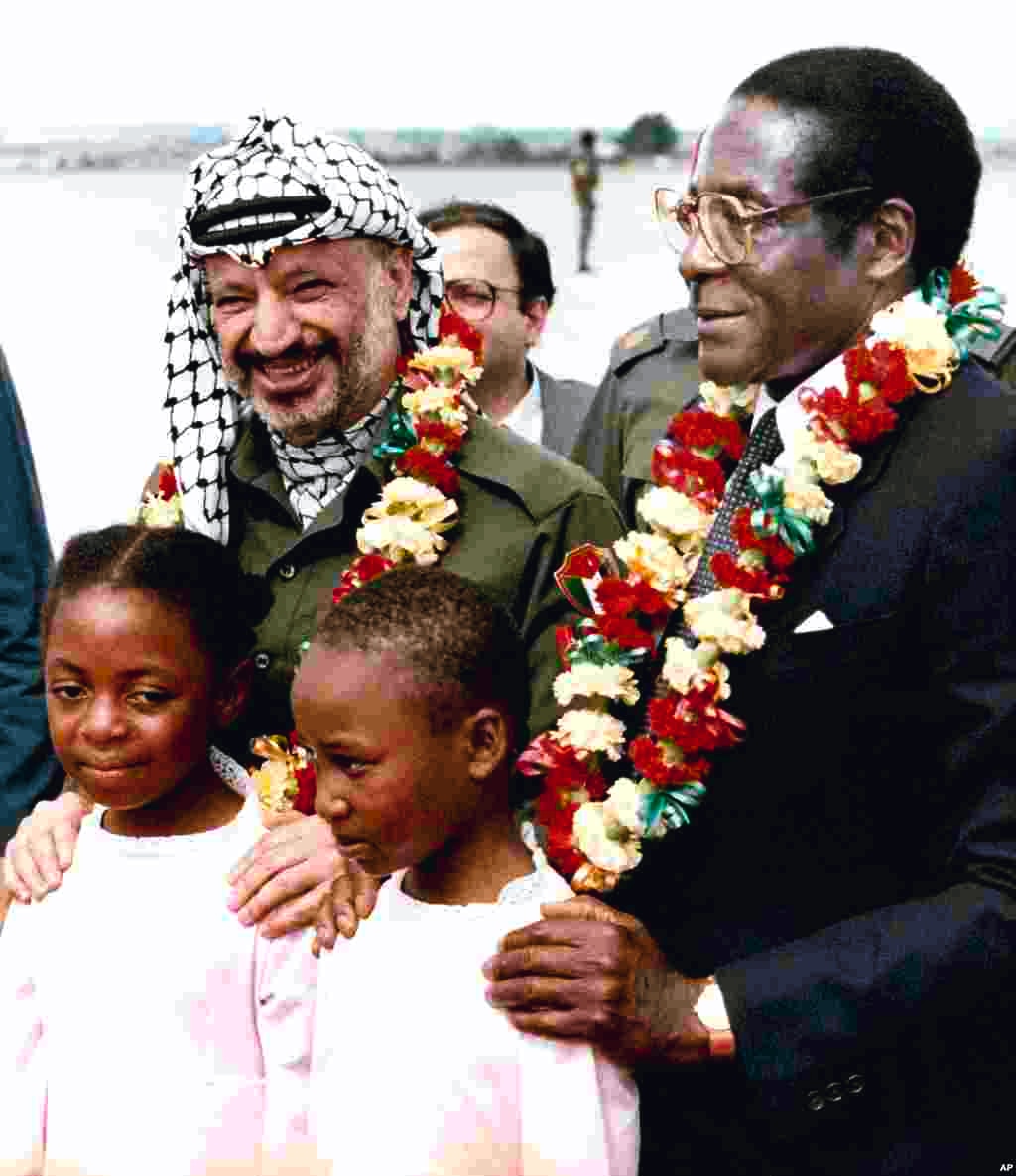 Perdana Menteri Zimbabwe Robert Mugabe, kanan, dan Yasser Arafat, kiri, berfoto setelah menerima kalung bunga dari dua siswi berumur 10 tahun, Jean Chitanda, kiri, dan Tsitsi Chikasha, pada saat Arafat tiba di Bandara Harare, Zimbabwe, 14 April 1987, untuk menghadiri Komite Gerakan Non-Blok mengenai Palestina. (AP Photo)