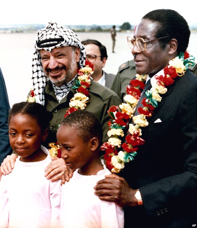 Zimbabwean Prime Minister Robert Mugabe, right, and Yasser Arafat, left, pose for photos after being garlanded by two 10-year-old school girls, Jean Chitanda, left, and Tsitsi Chikasha, on Arafat's arrival at Harare Airport, Zimbabwe, April 14, 1987, to attend a meeting of the Non-aligned Movement's Committee on Palestine. (AP Photo)