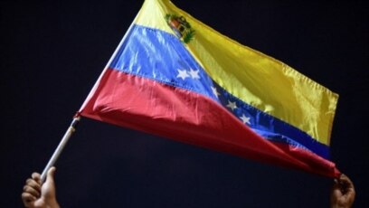 Un hombre muestra una bandera venezolana mientras familiares y amigos de migrantes venezolanos que murieron cuando un bote que los transportaba a Trinidad y Tobago se hundió, protesta en Güiria, Venezuela, el 18 de diciembre de 2020.