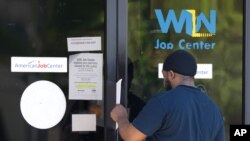 FILE - A man is handed an unemployment benefit application form by a security guard from behind glass doors of a state WIN Job Center in north Jackson, Mississippi, April 2, 2020. 