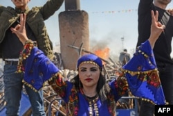 FILE - A young woman flashes the victory sign in front of a bonfire as Turkish Kurds gather during Newroz celebrations for the new year in Diyarbakir, southeastern Turkey, on March 21, 2018.