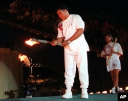 FILE - In this July 19, 1996, file photo, American swimmer Janet Evans looks on as Muhammad Ali lights the Olympic flame during the 1996 Summer Olympic Games opening ceremony in Atlanta.